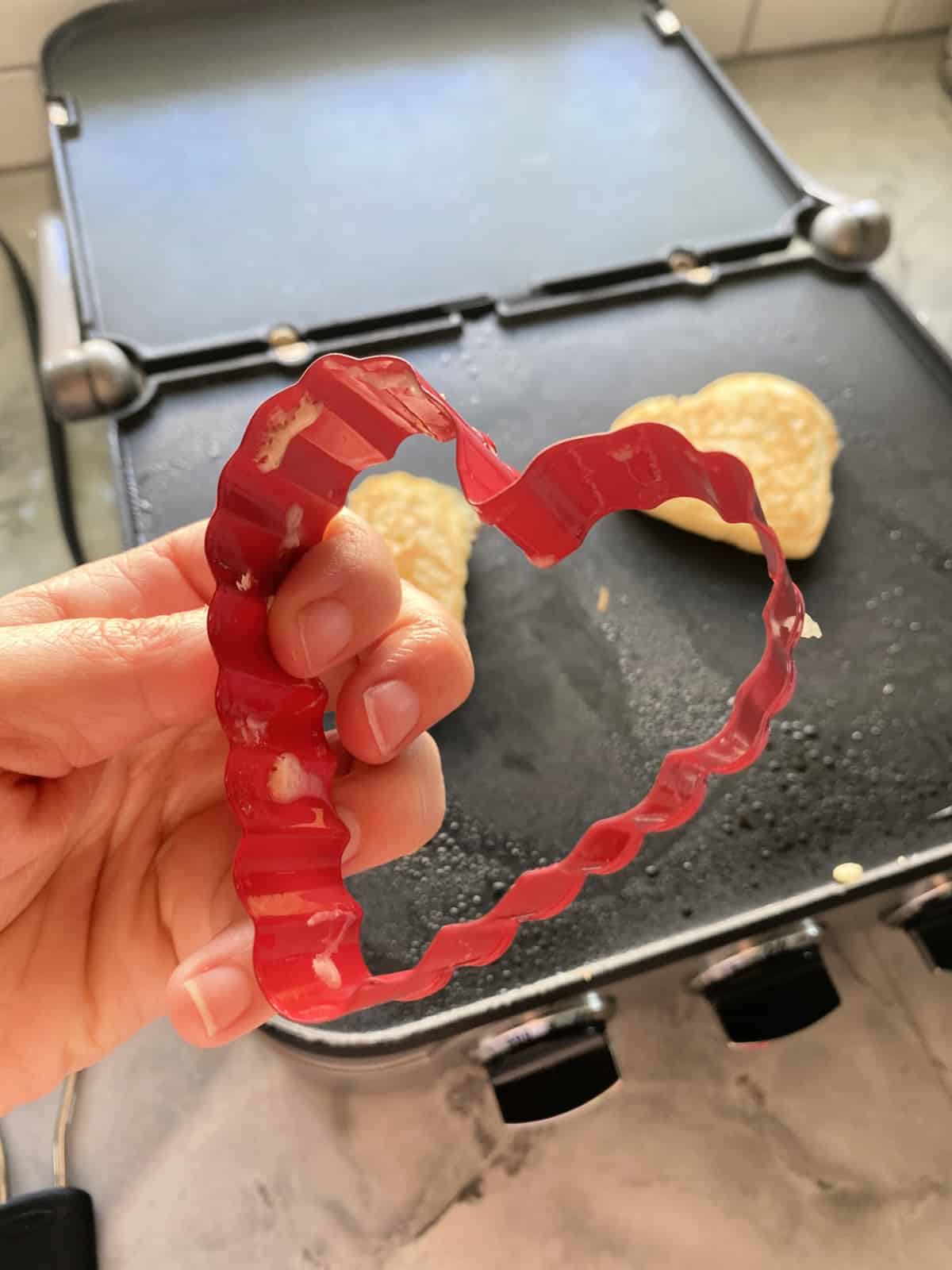 Hand holding heart shaped cookie cutter with batter stuck on the sides.