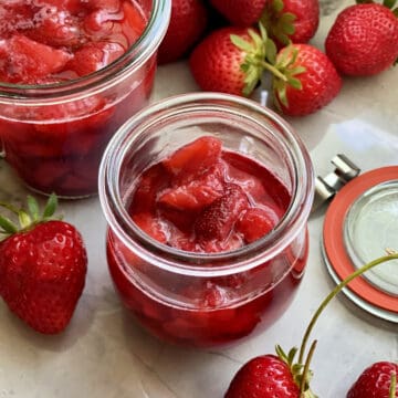 Glass jar filled with strawberry sauce and strawberries on the side.