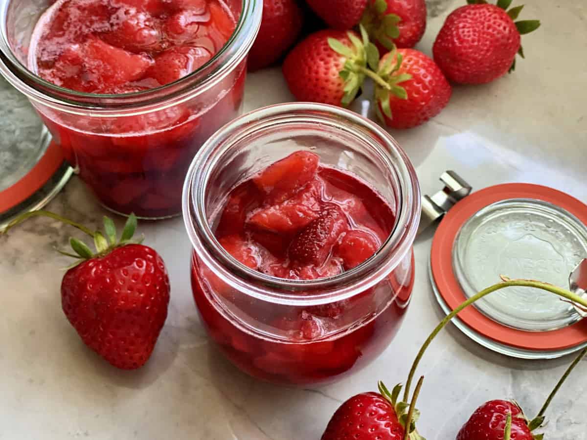 Glass jar filled with strawberry sauce and strawberries on the side.