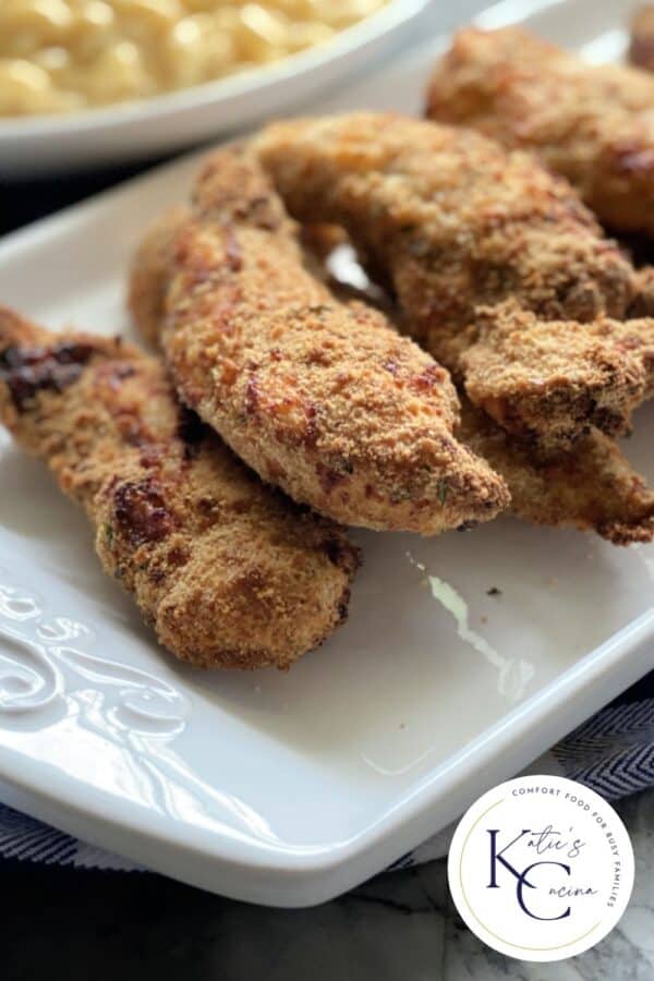 5 chicken strips stacked on a white platter with logo on right bottom corner.