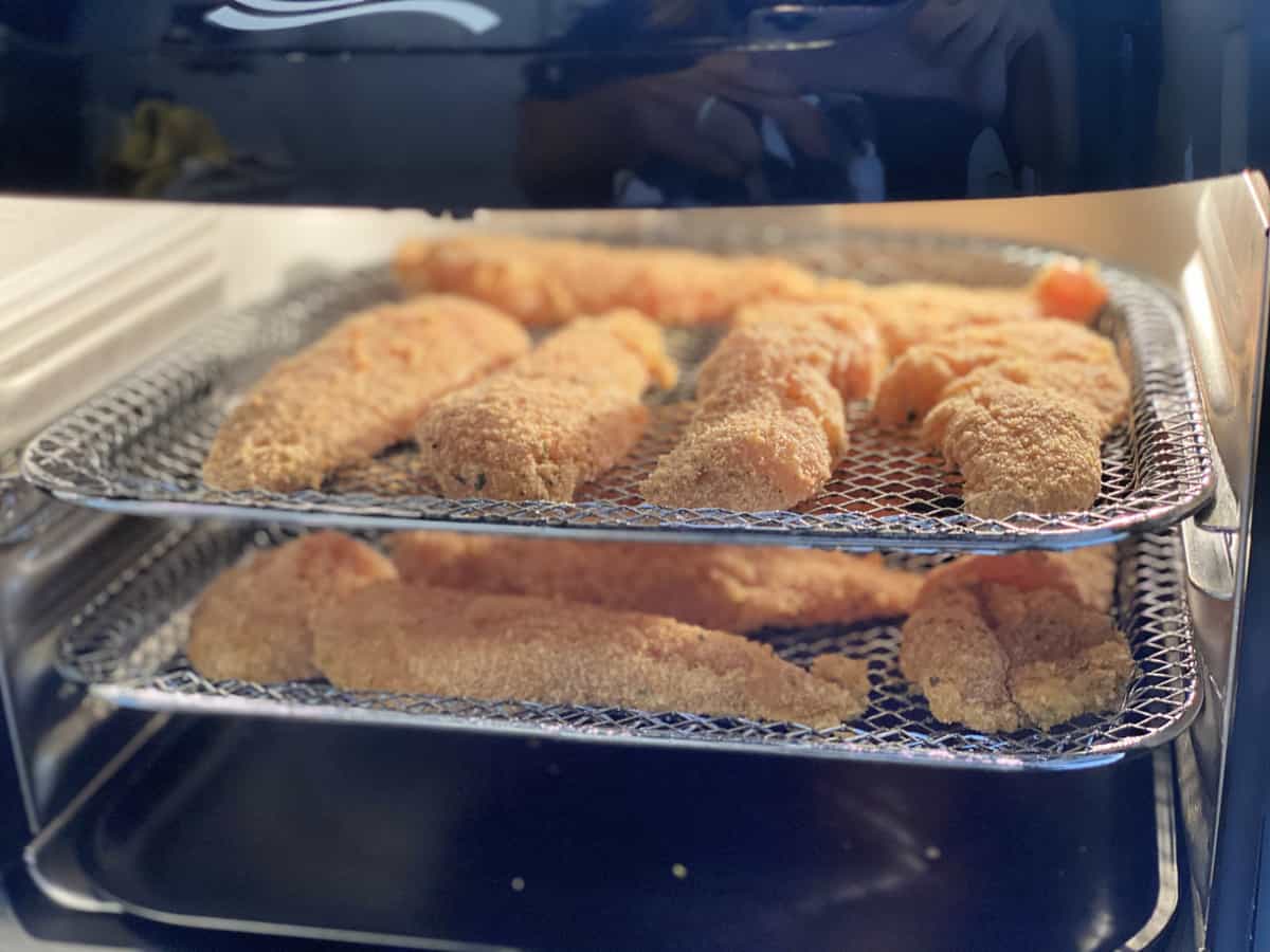 Breaded chicken tenderloins on a wire rack inside an air fryer.