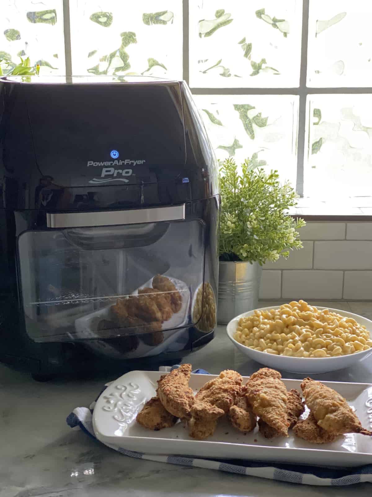 White platter filled with stacked chicken tenders with mac and cheese and Air Fryer in the background.