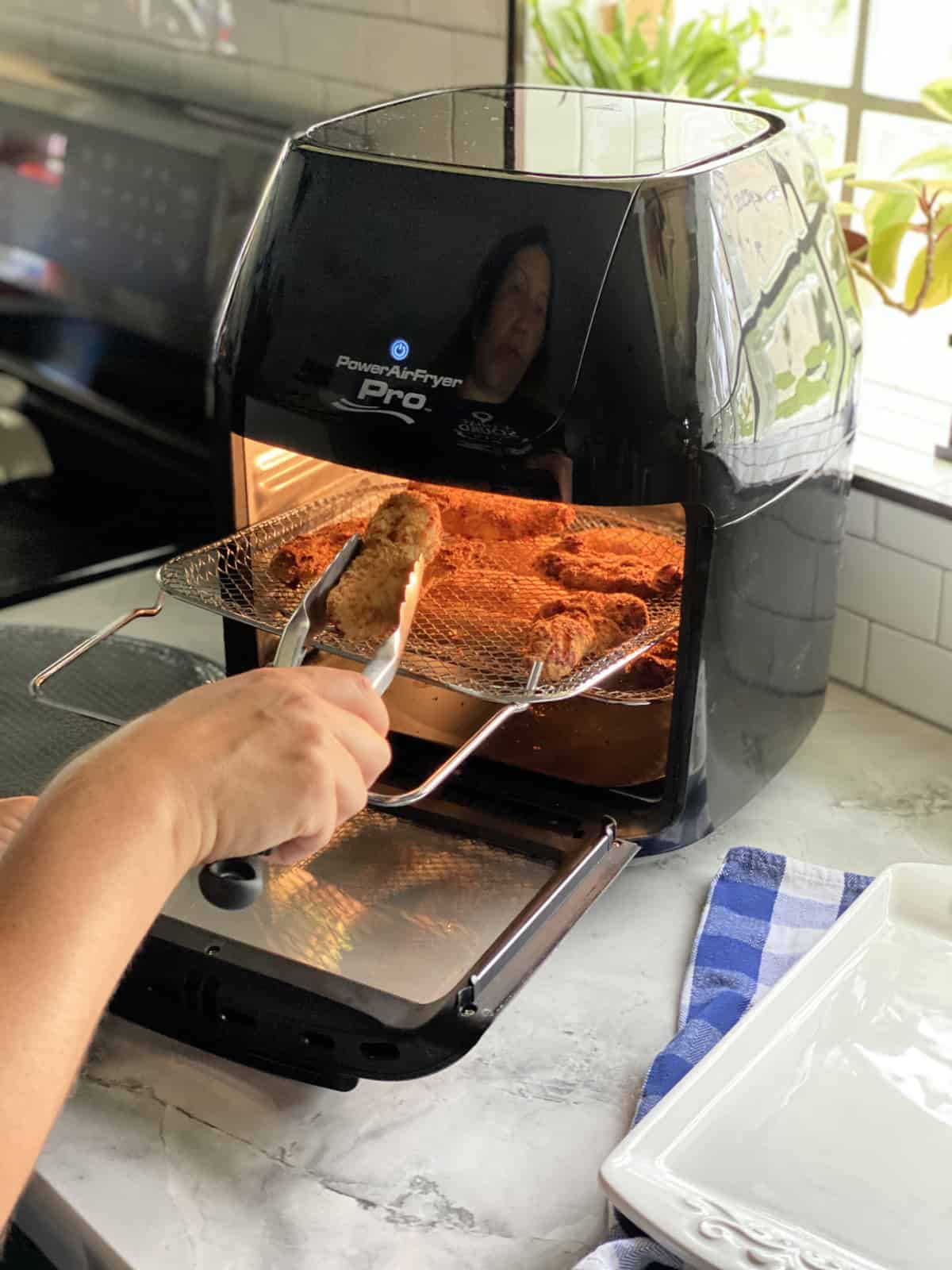 Female hand holding tongs pulling out chicken strips out of Air Fryer.