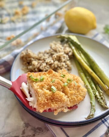 Red spatula placing a piece of breaded fish onto a plate with rice and asparagus.