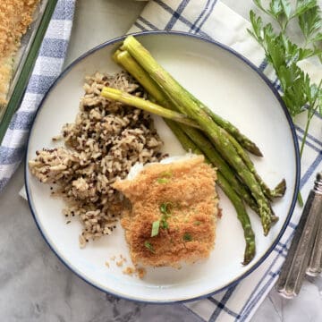 Top view of a piece of breaded fish on a white plate filled with wild rice and asparagus.