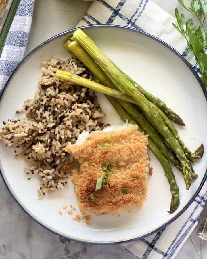 Top view of a piece of breaded fish on a white plate filled with wild rice and asparagus.