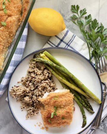 Top view of a white plate with breaded fish, asparagus, and wild rice.