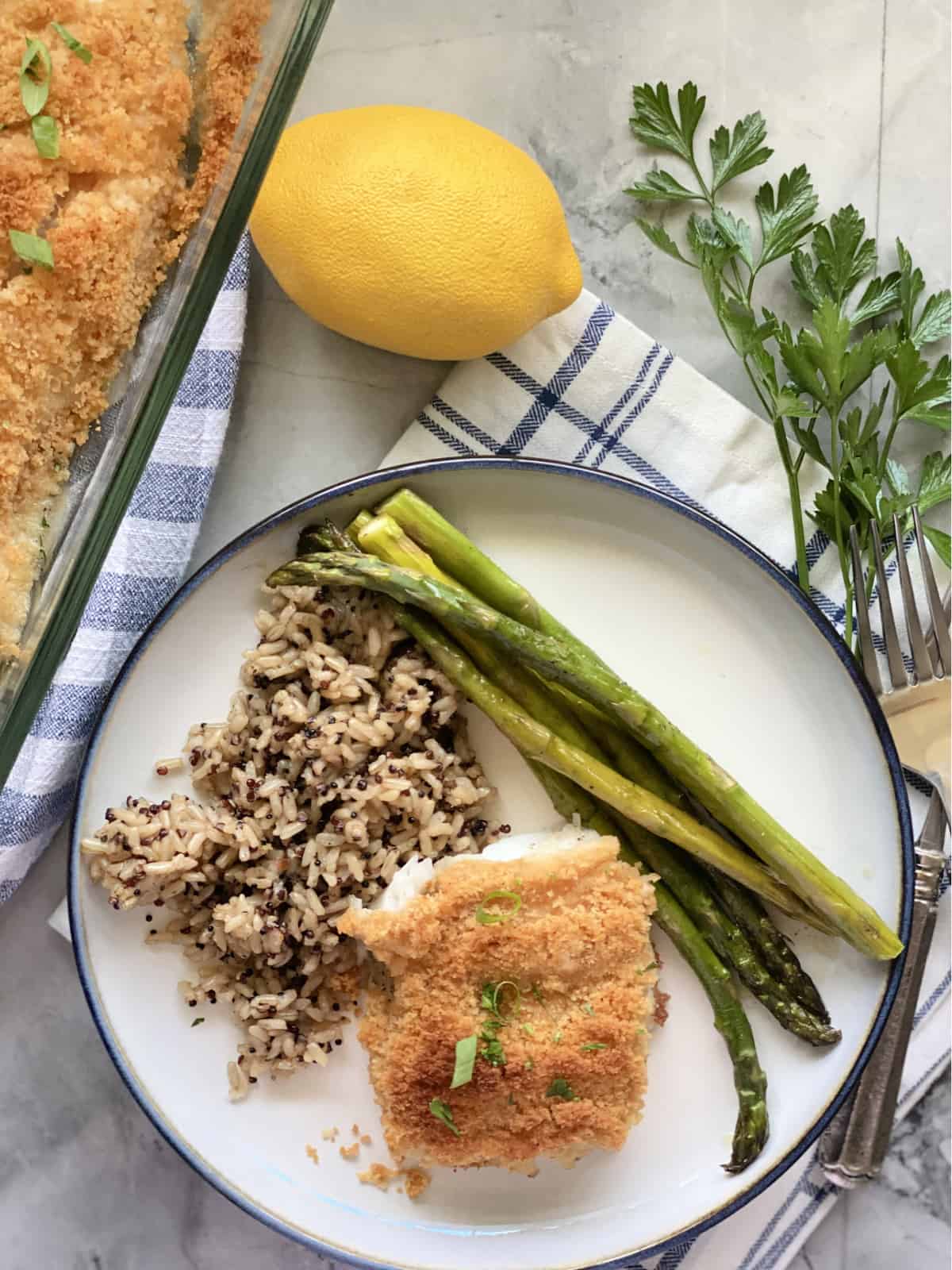 Top view of a white plate with breaded fish, asparagus, and wild rice.