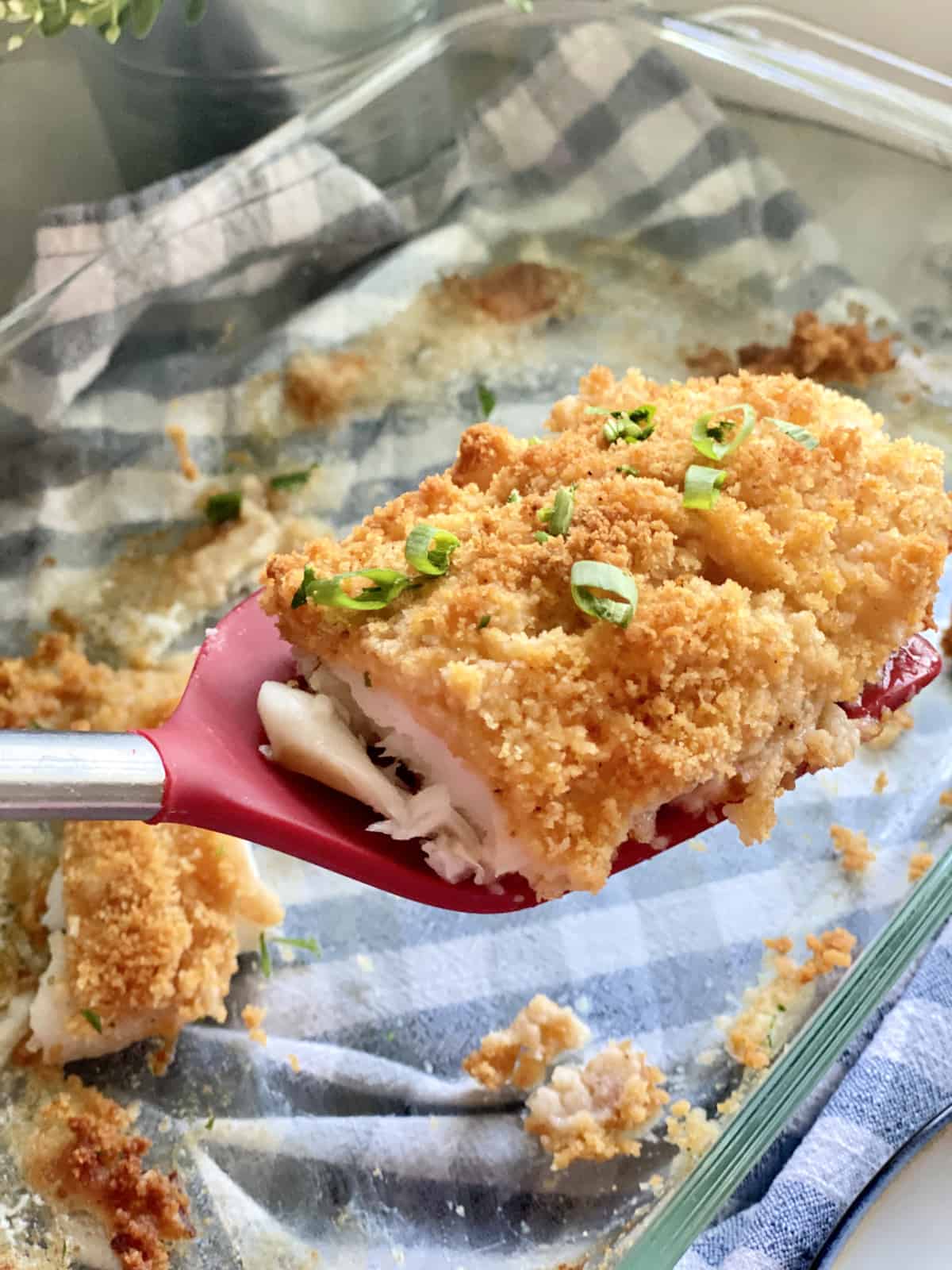 Red spatula with a piece of breaded fish on top.