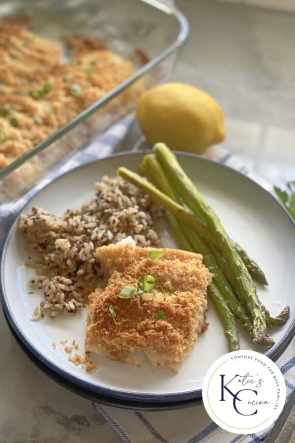 White plate filled with fish, rice, and asparagus with logo on right corner.