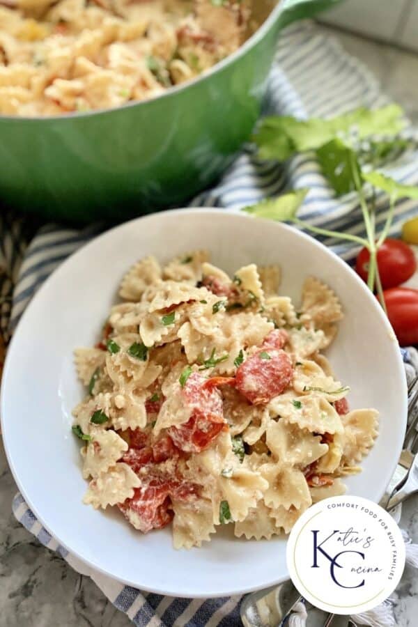 White bowl filled with creamy bowtie pasta with logo on right corner.