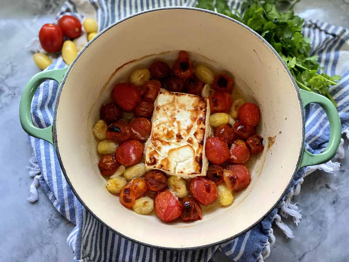 Top view of baked feta with blistered tomatoes in a green pot.