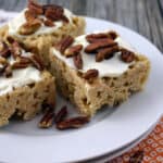 White plate with rice krispies treats stacked topped with frosting and chopped pecans.