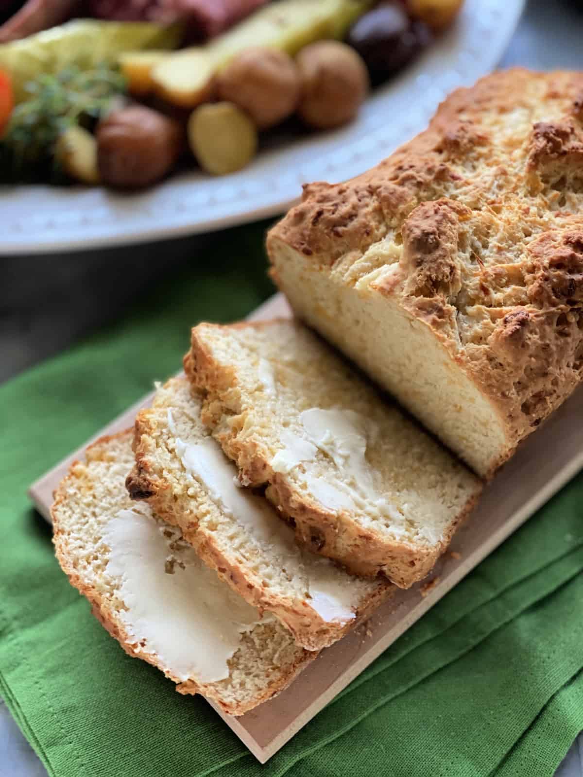 Loaf of bread on a wood cutting board with three buttered slices.