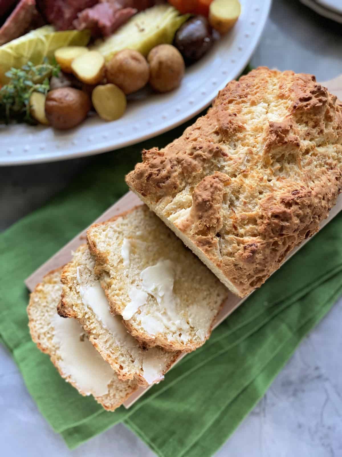 Close up of three buttered slices of bread on a wood cutting board sitting on a green cloth.