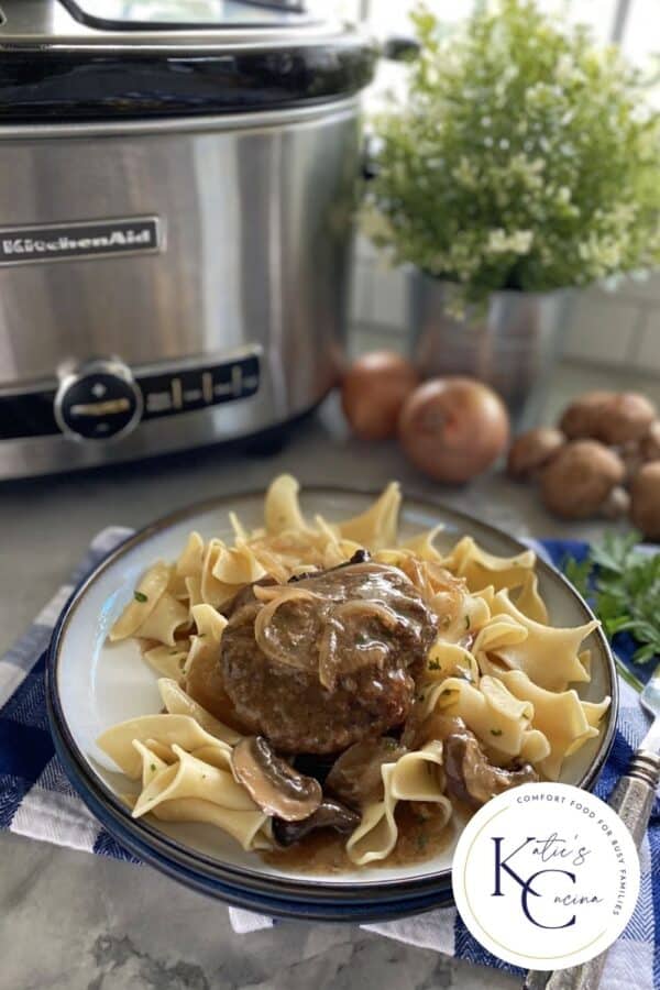 White plate filled with noodles, steak, and gravy with a logo on the right corner.