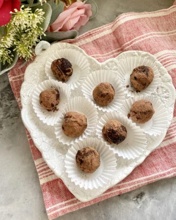 Top view of heart shaped plate filled with 8 truffles sitting on a red and white stripped cloth.