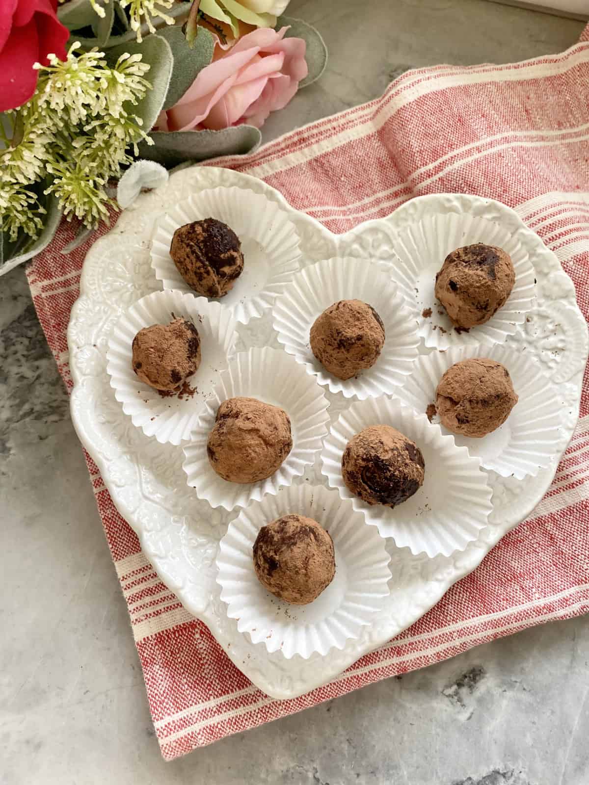 Top view of heart shaped plate filled with 8 truffles sitting on a red and white stripped cloth.