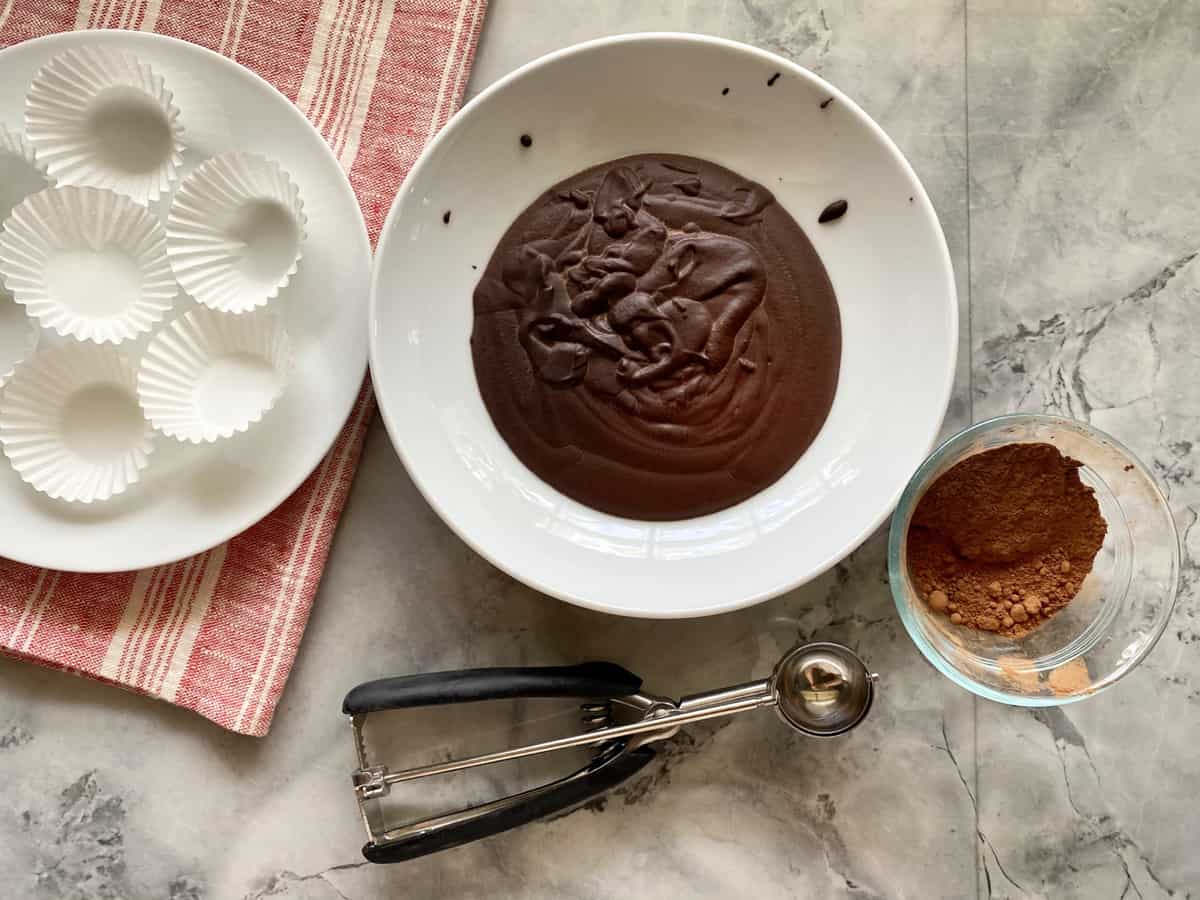 Top view of a bowl of hardend chocolate ganache, wrappers, cookie scoop, and cocoa powder.