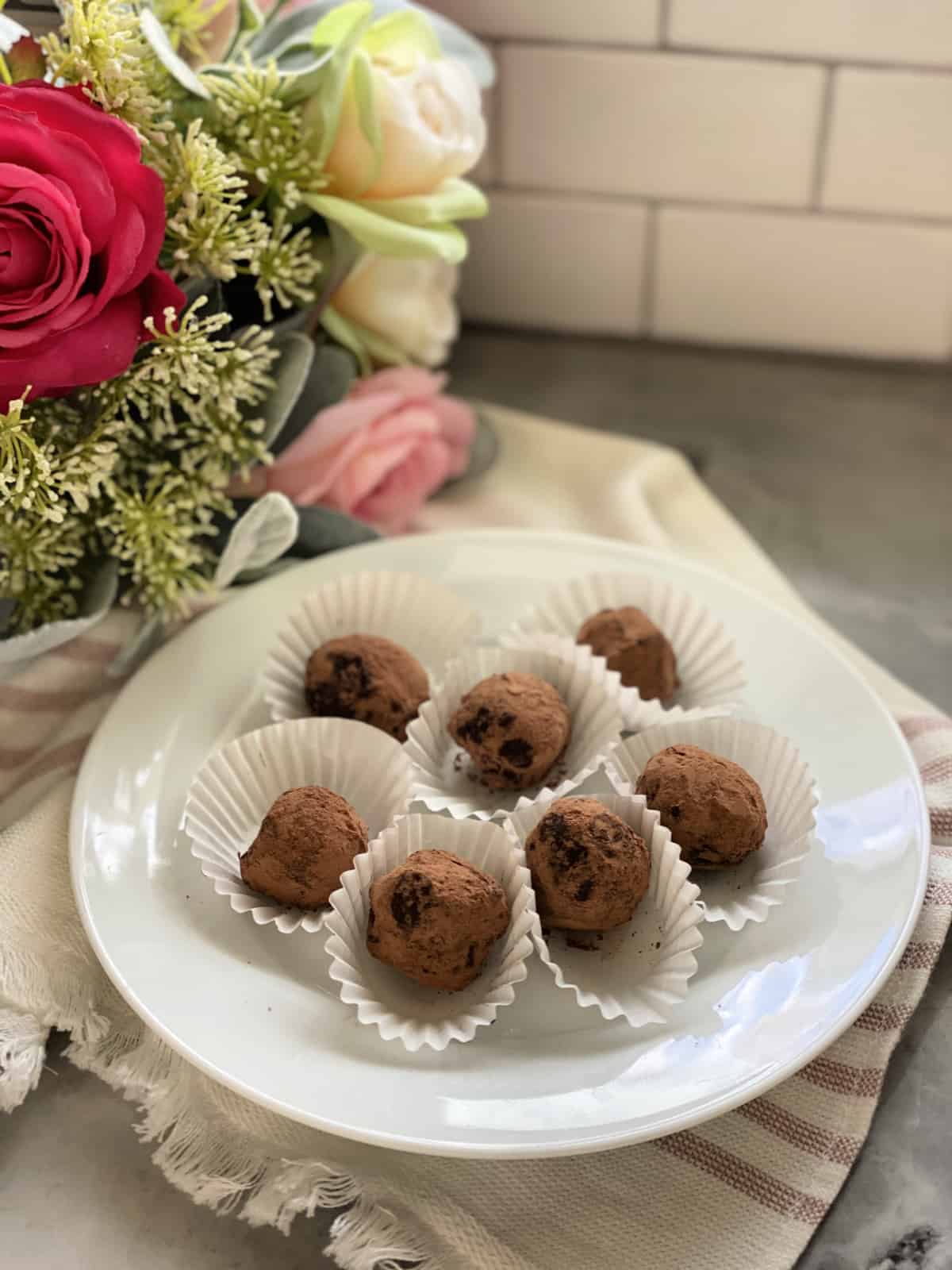 White plate filled with 7 cocoa dusted chocolate truffles with roses in background.