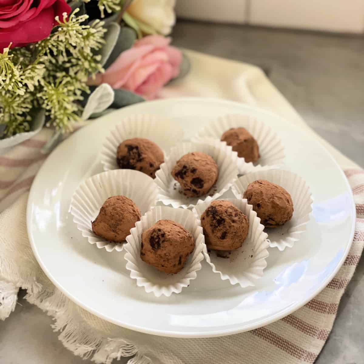 White plate filled with 6 chocolate truffles in white liners.