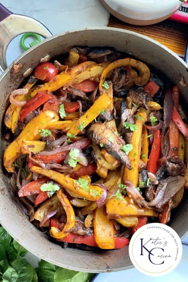 Top view of a skillet with peppers, onions, and mushrooms.