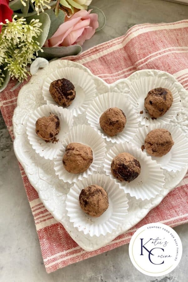 Top view of a heart shaped plate filled with 8 Dark Chocolate Truffles with roses next to it.