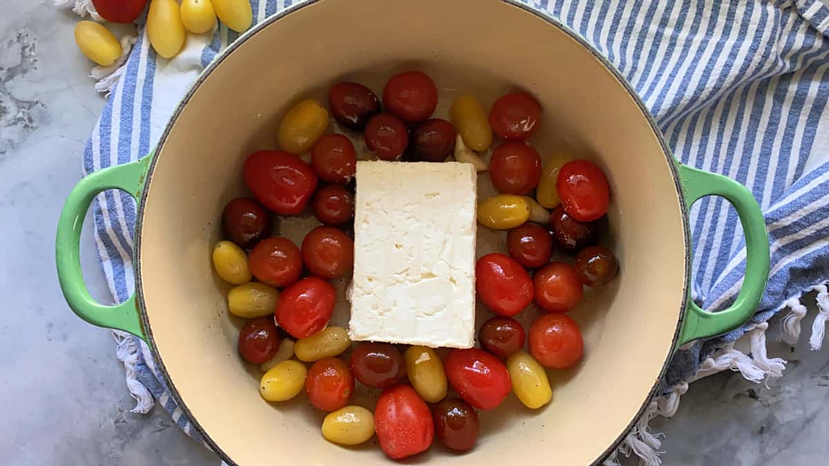 Top view of a block of feta with grape tomatoes in a green pot.