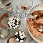 Top view of a bowl of hot chocolate mix with mason jars filled with mix plus marshmallows and chocolate chips.