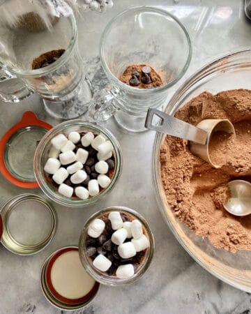 Top view of a bowl of hot chocolate mix with mason jars filled with mix plus marshmallows and chocolate chips.