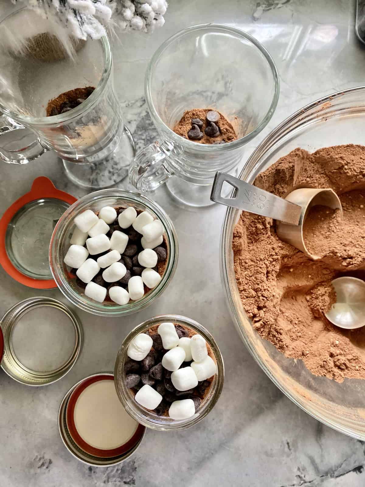 Top view of a bowl of hot chocolate mix with mason jars filled with mix plus marshmallows and chocolate chips.