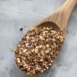 Top view of a wooden spoon on a marble countertop filled with seasoning.