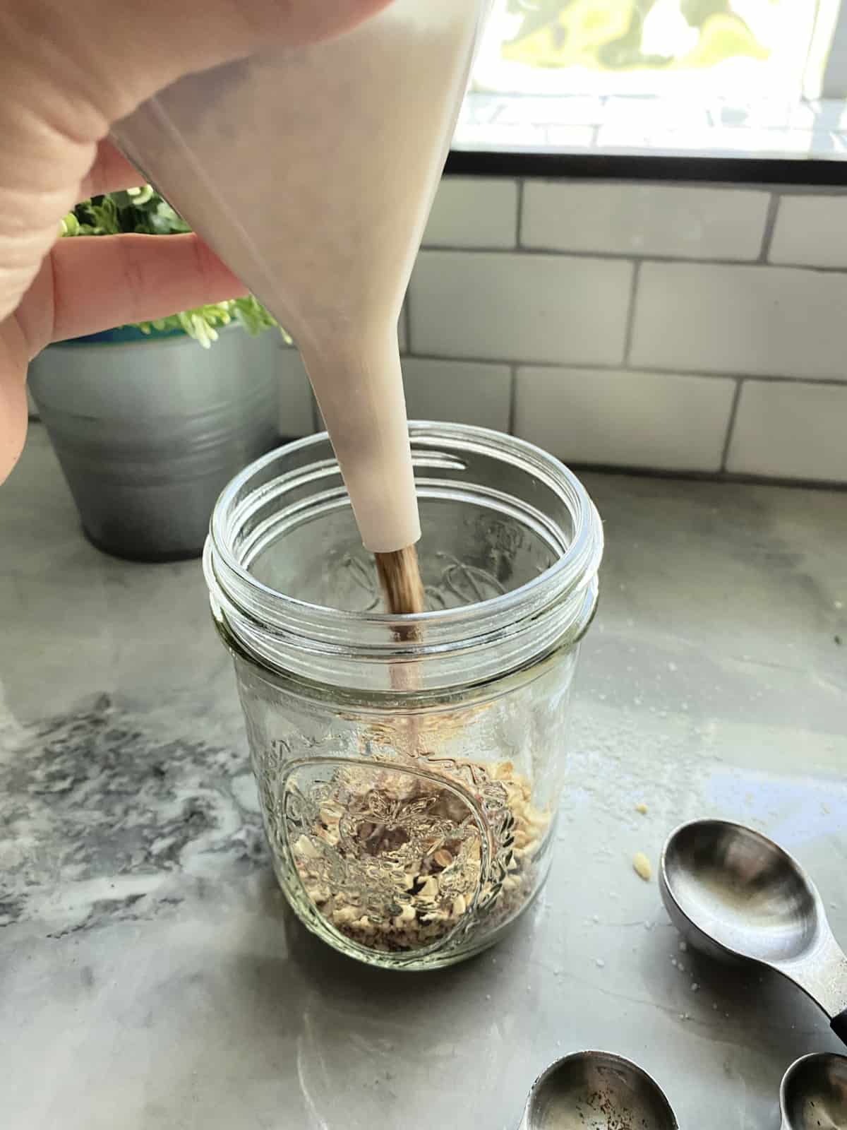 Hand holding a funnel that is pouring spices into a mason jar.