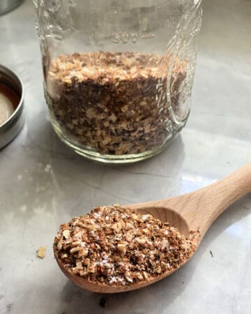 Wooden spoon filled with spices with a mason jar filled with spices in the background.