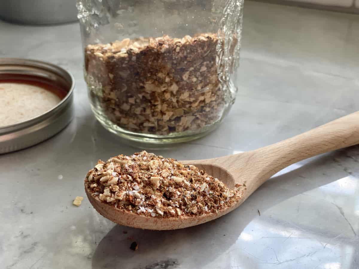 Wooden spoon filled with seasoning with a mason jar filled with spices in the background.