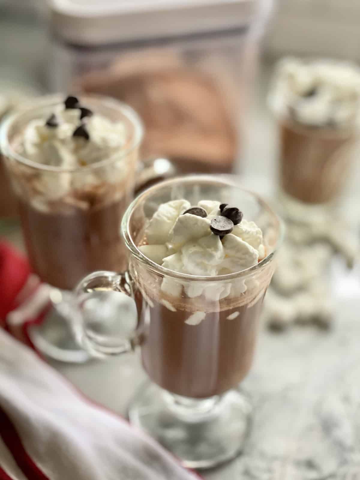 Two glasses of hot chocoalte topped with whipped cream and chocolate chips.