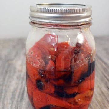 Glass canning jar with silver lid filled with roasted red bell peppers.