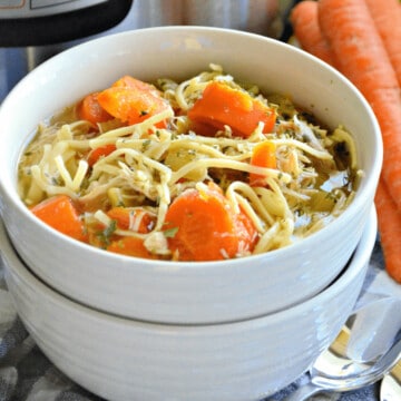 Two white bowls stacked with carrots, noodles and chicken with broth.