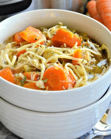 Two white bowls stacked with carrots, noodles and chicken with broth.
