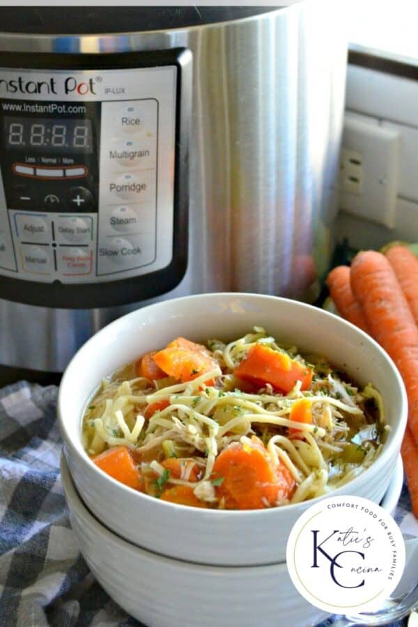 Two white bowls stacked with top bowl filled with chicken noodle soup with carrots and Instant Pot in the background.