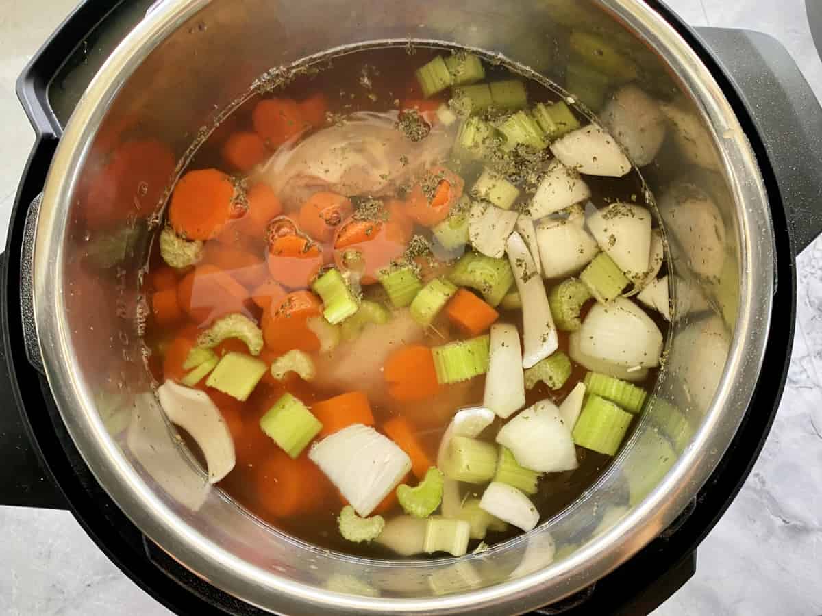 Top view of an instant pot with raw carrots, celery, and onions chopped.
