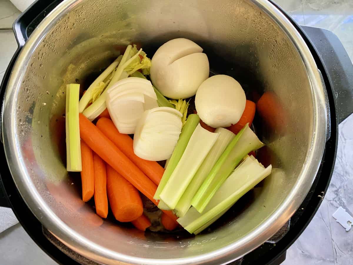 Top view of an Instant Pot filled with fresh carrots, chopped celery and onions.