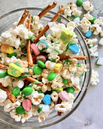 Top view of a glass bowl filled with a snack mix of popcorn, candies, and pretzels.