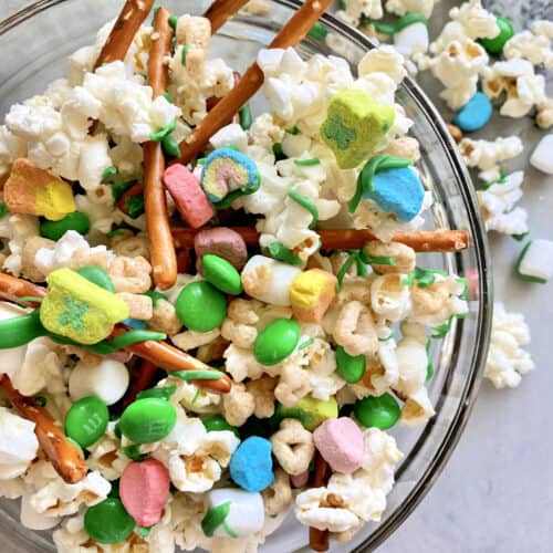 Top view of a glass bowl filled with a snack mix of popcorn, candies, and pretzels.