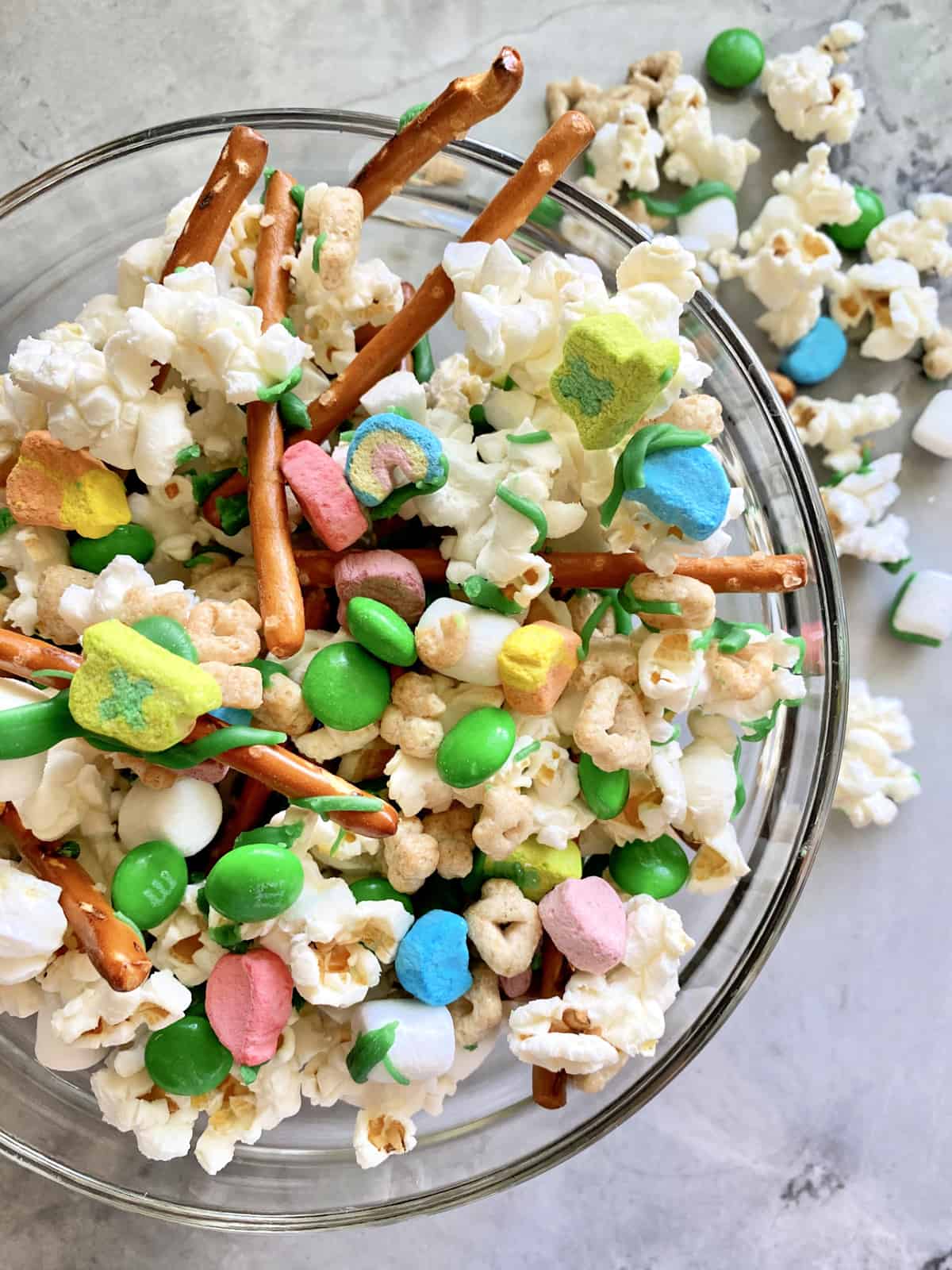 Top view of a glass bowl filled with a snack mix of popcorn, candies, and pretzels.