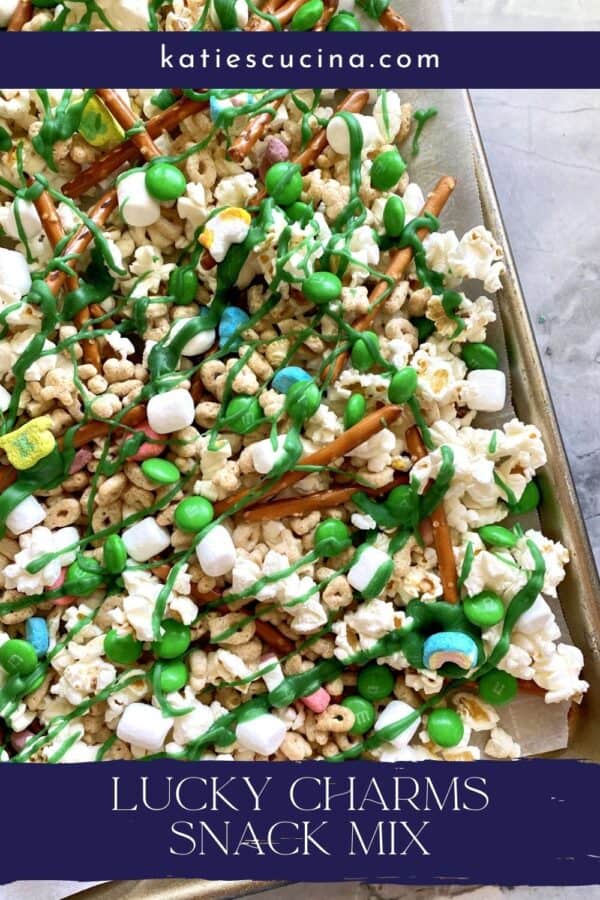 Top view of a baking tray filled with popcorn, pretzels, M&M's, and Lucky Charms with green white chocolate splattered on top.