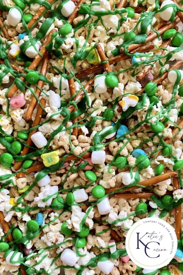 Close up of popcorn, pretzel, M&M's, and with Lucky Charms spread on a tray with logo on the right corner.