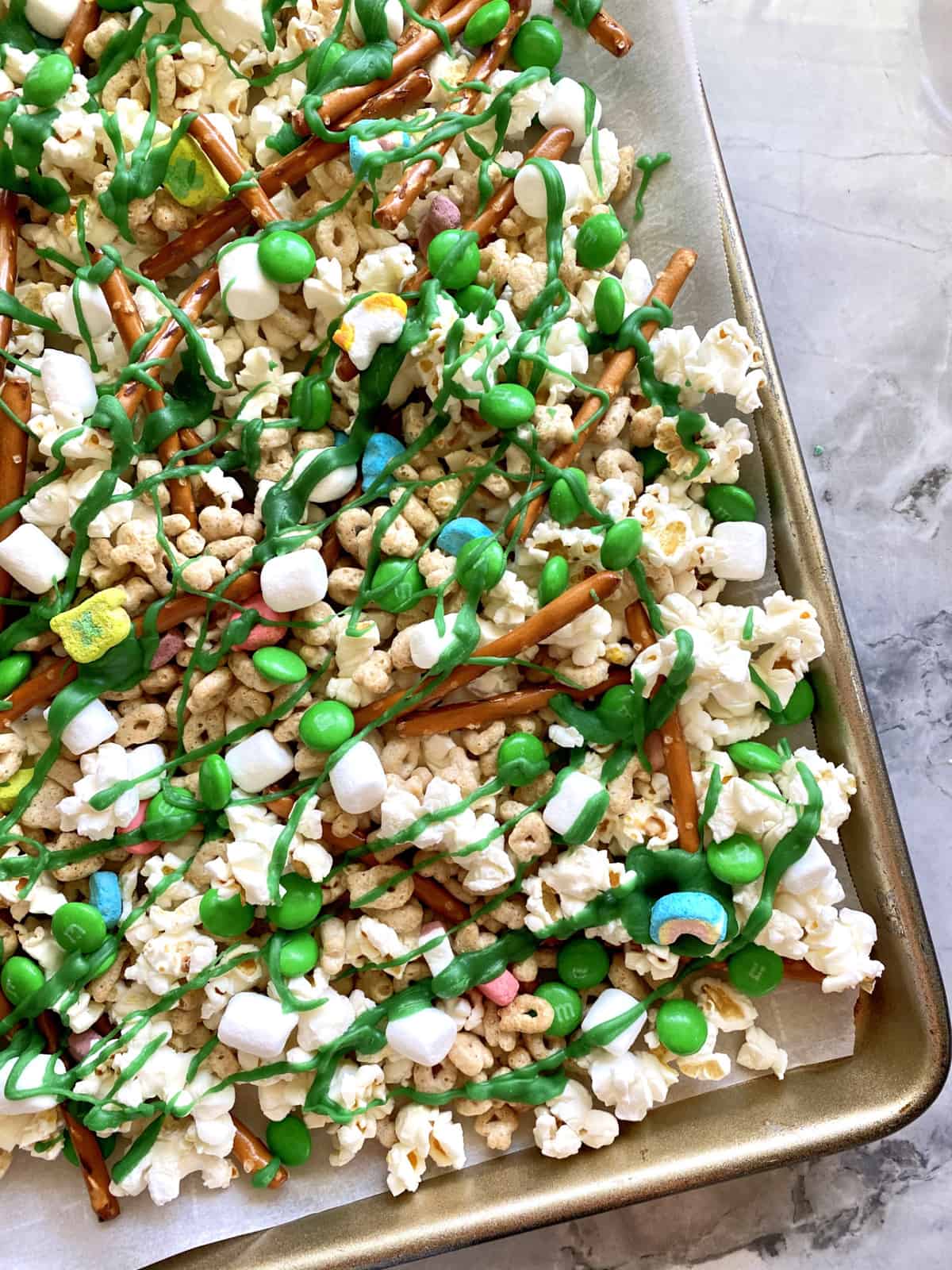 Top view of a baking tray with popcorn, pretzels, and M&M's with white chocolate on top.