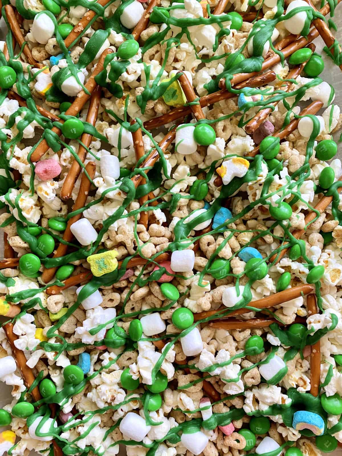 Close up of popcorn snack mix, pretzels, M&M's, and Lucky Charms Cereal.
