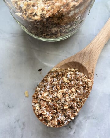 Top view of a wooden spoon filled with spices and a jar next to it.